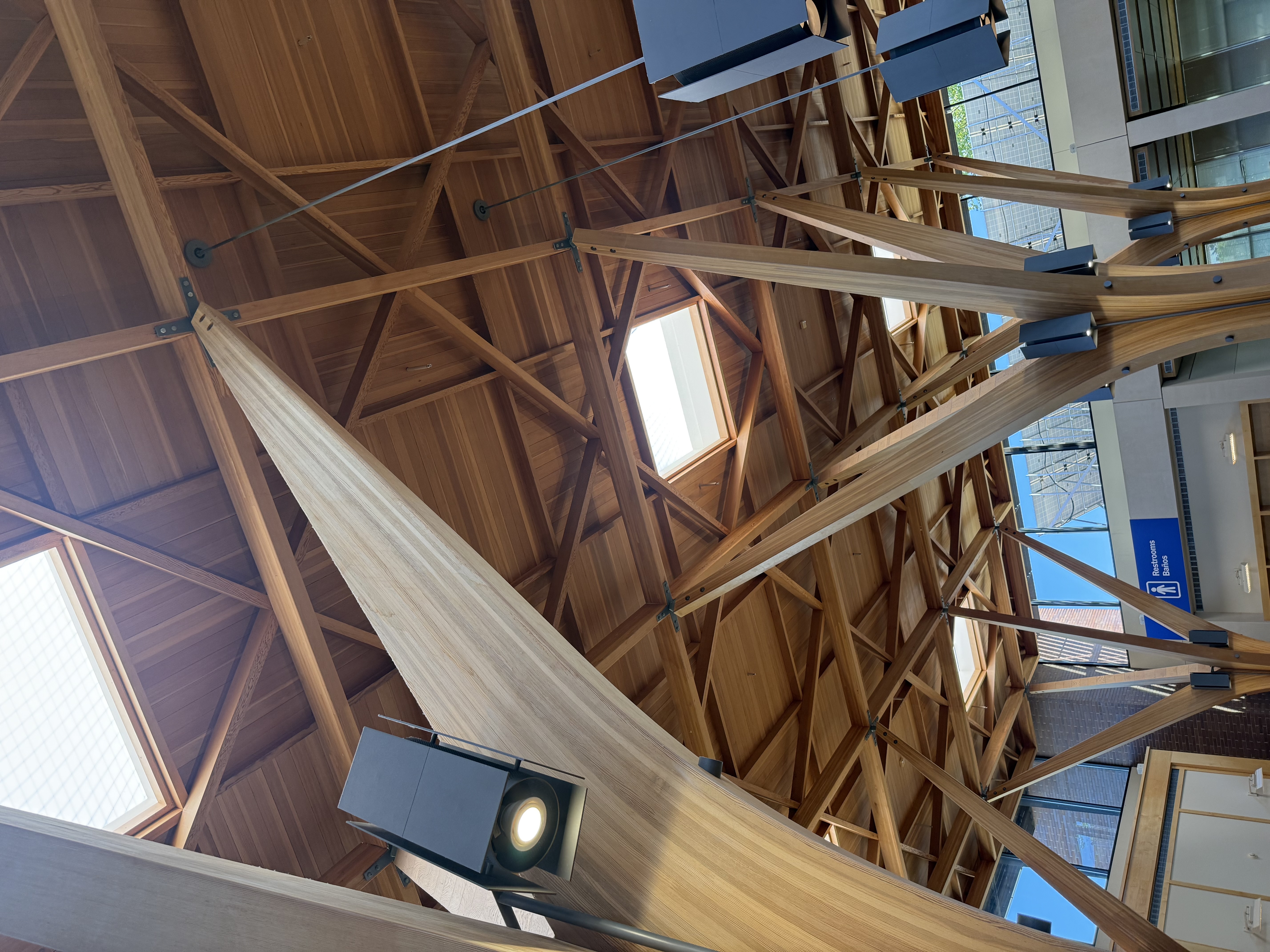 Close-up of the glulam structural connections — diagonal members meeting at a node with steel cable tension system and pendant light