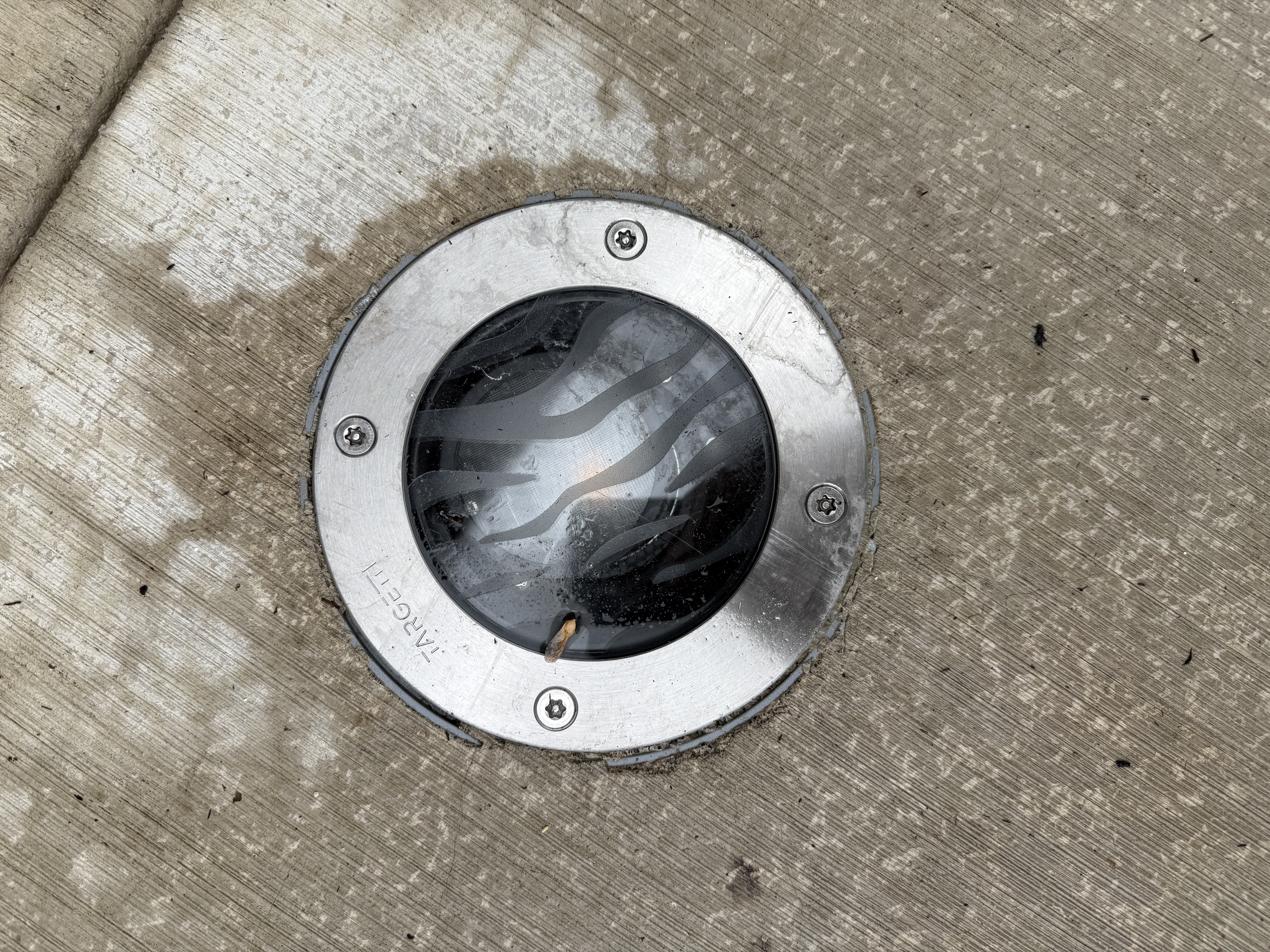 Close-up of a Targetti brand flush-mount in-grade light fixture embedded in the concrete patio surface
