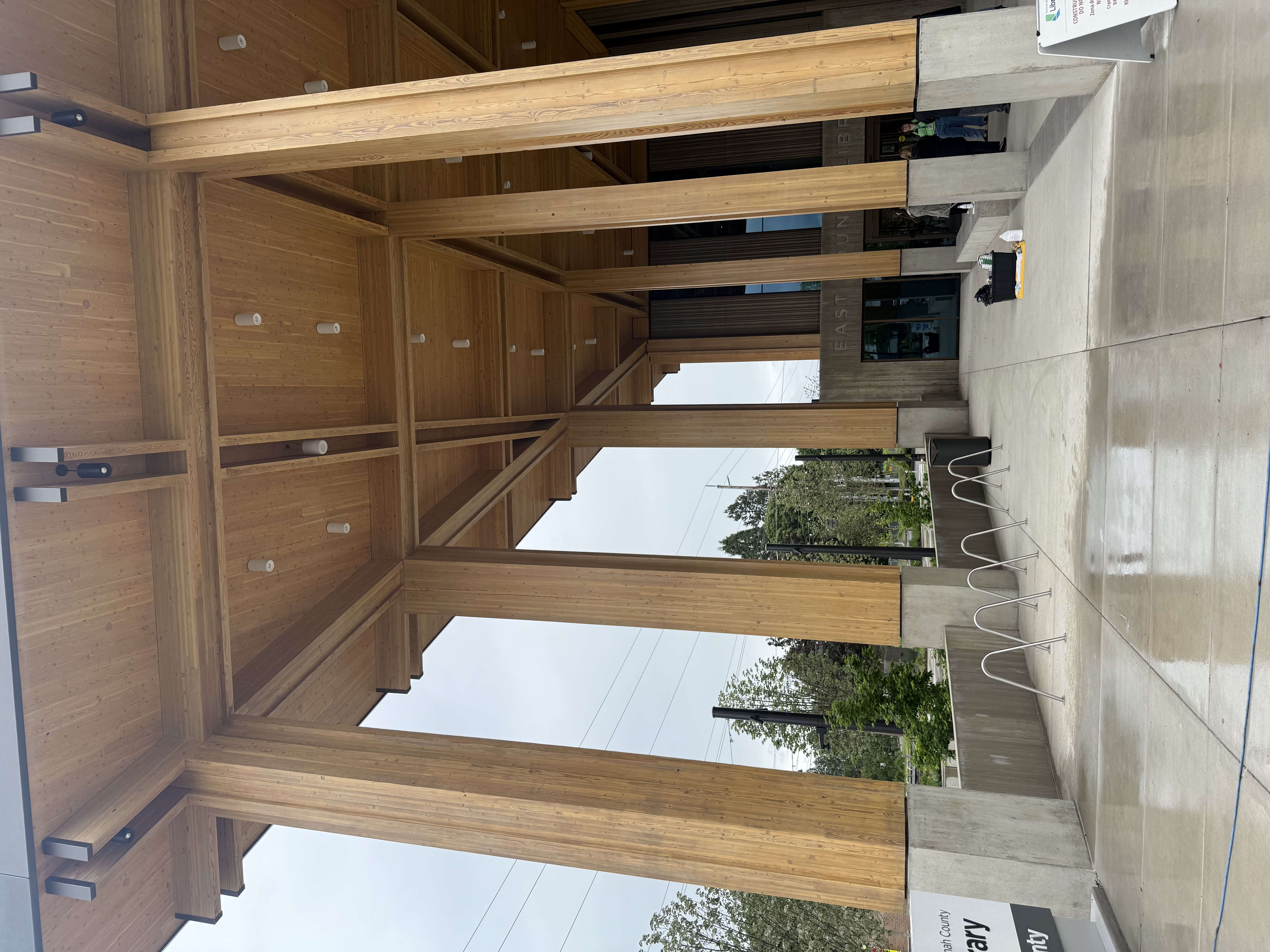 Interior view looking up at the timber frame pavilion structure showing glulam columns and wood-slat ceiling