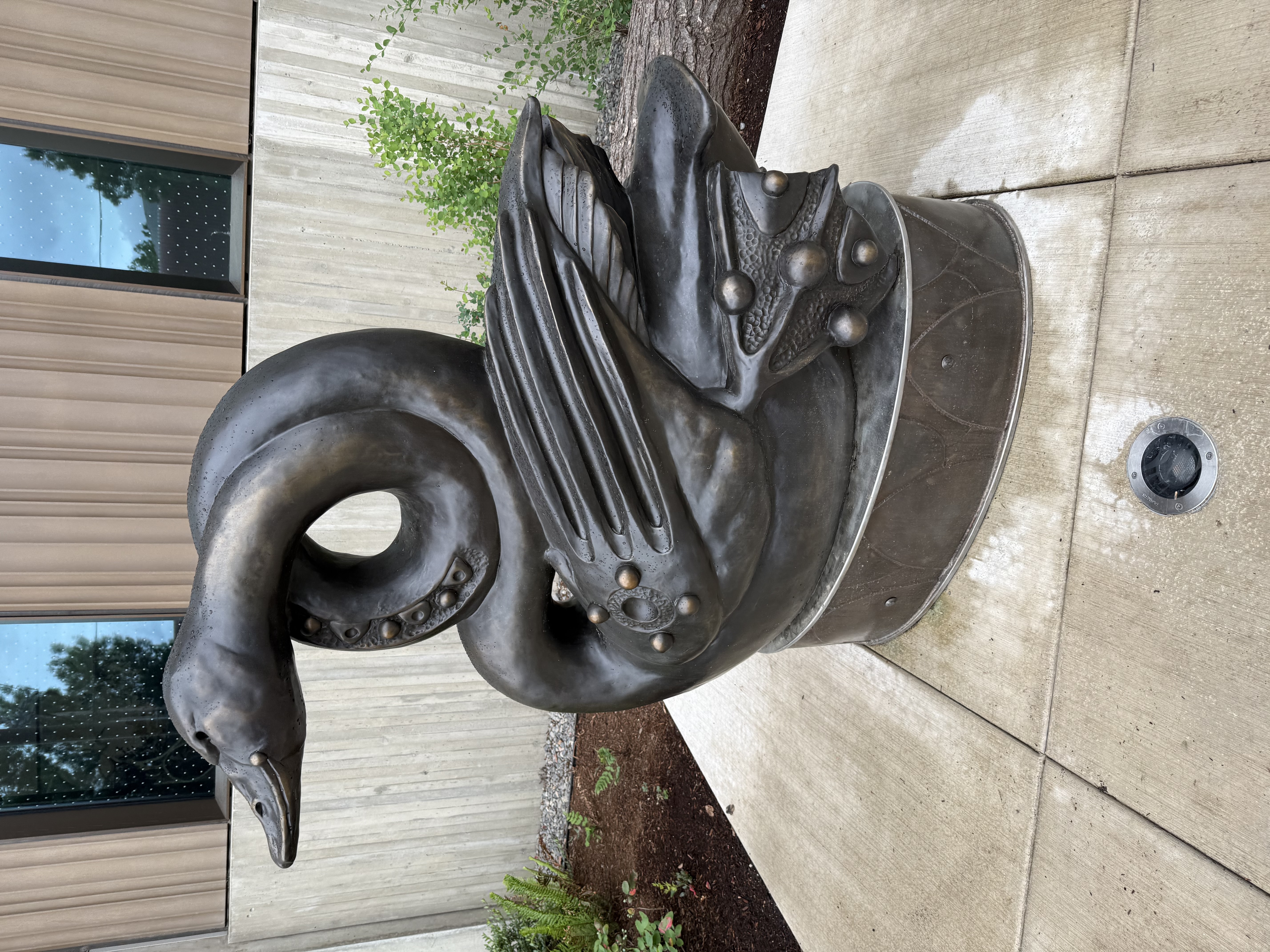 Large bronze bird sculpture — a stylized waterfowl or heron — on a concrete plinth outside the library entrance